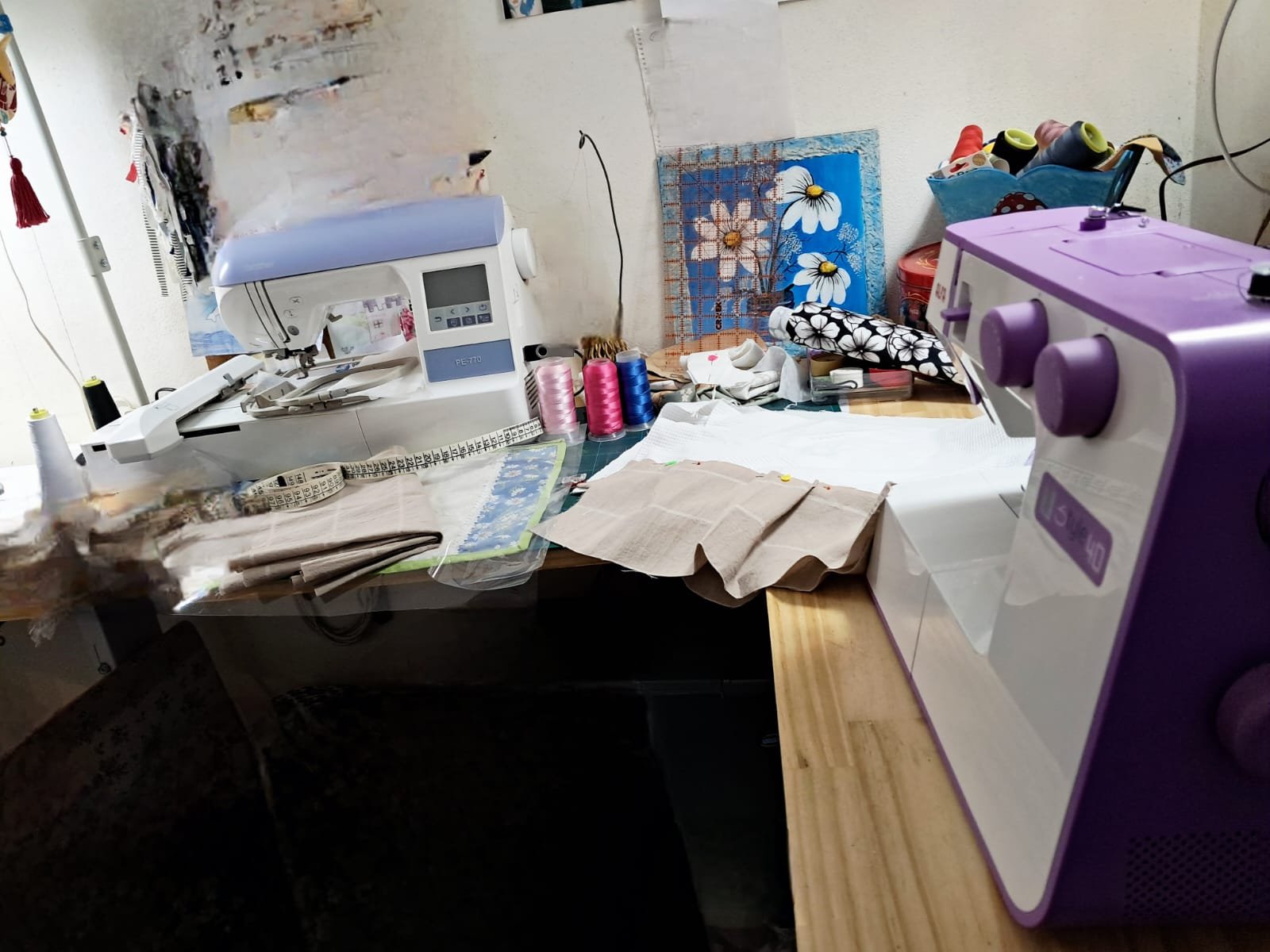 Mesa de trabajo en el taller de Lo de Sabri con dos máquinas de coser, telas, carretes y cinta métrica